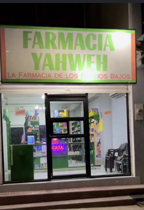 Fachada de una sucursal de Farmacia Yahweh, con su rótulo verde iluminado